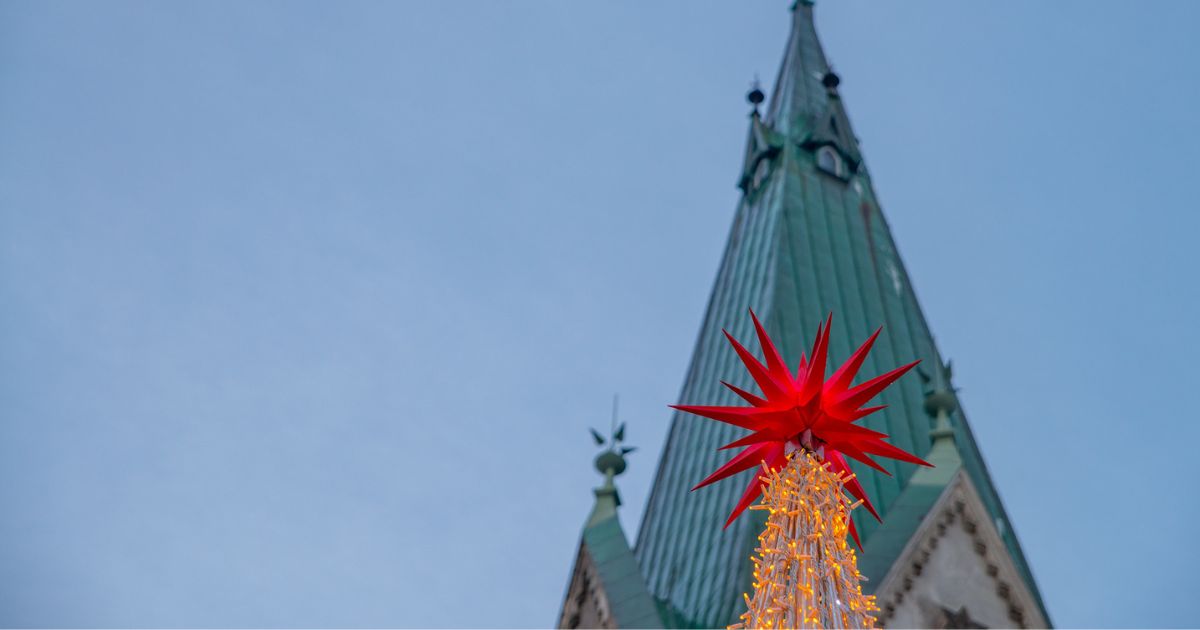 Julebilde med en julestjerne i tippen av et tre som ligger foran kirkespiret på Domkirka.