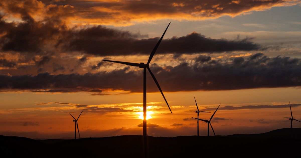 Bilde av vindturbiner med skyer og sol i bakgrunnen.